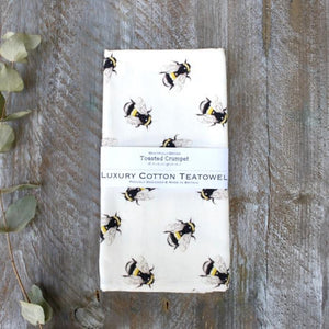 bee print on a white cotton tea towel on a wooden background with eucalyptus stem